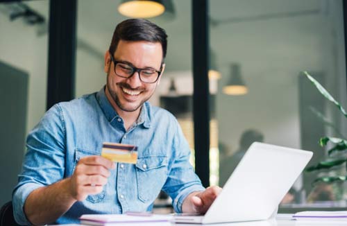 Man looking at this laptop holding a debit card