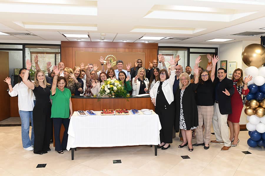 A group of Sunstate Bankers in the bank lobby with cake, waving at the camera