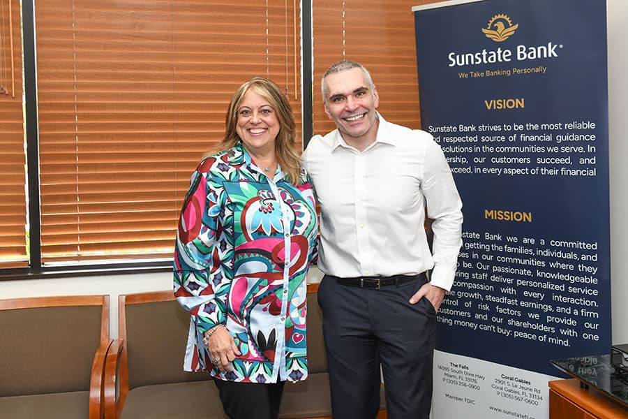 Two people posing in front of a Sunstate Bank Mission banner