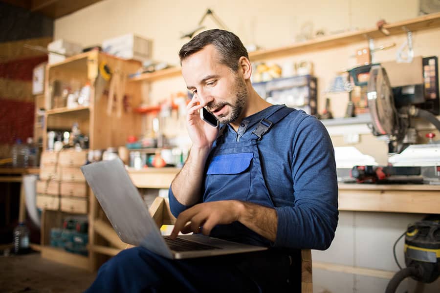 A man in his workshop in the phone while looking at his laptop