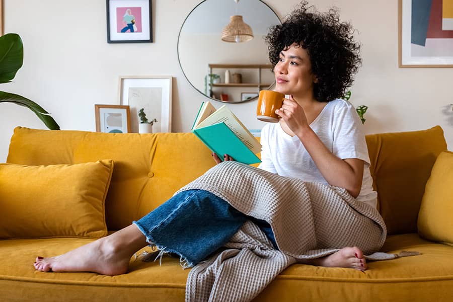 A woman relaxing on the couch with a book and a mug of tea